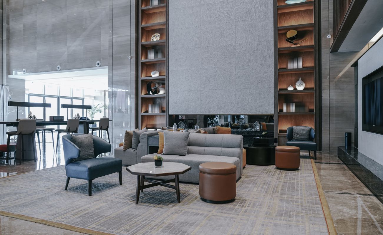Moderne Lobby mit einem grauen Sofa, einem runden Tisch, einem blauen Sessel und einem Teppich. Regale mit Dekorationsgegenständen im Hintergrund.